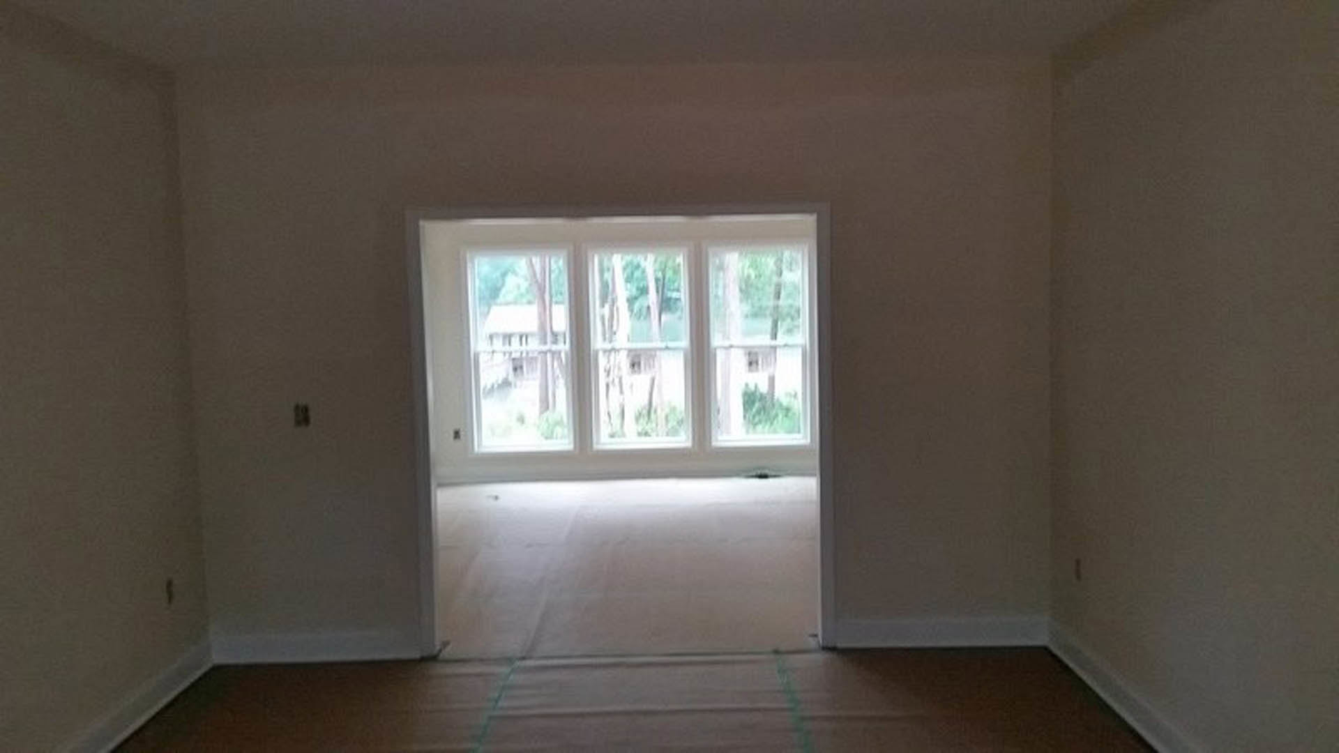 Bright room featuring a large window, white plaster walls, wood flooring, recessed ceiling lights, and a simple door.