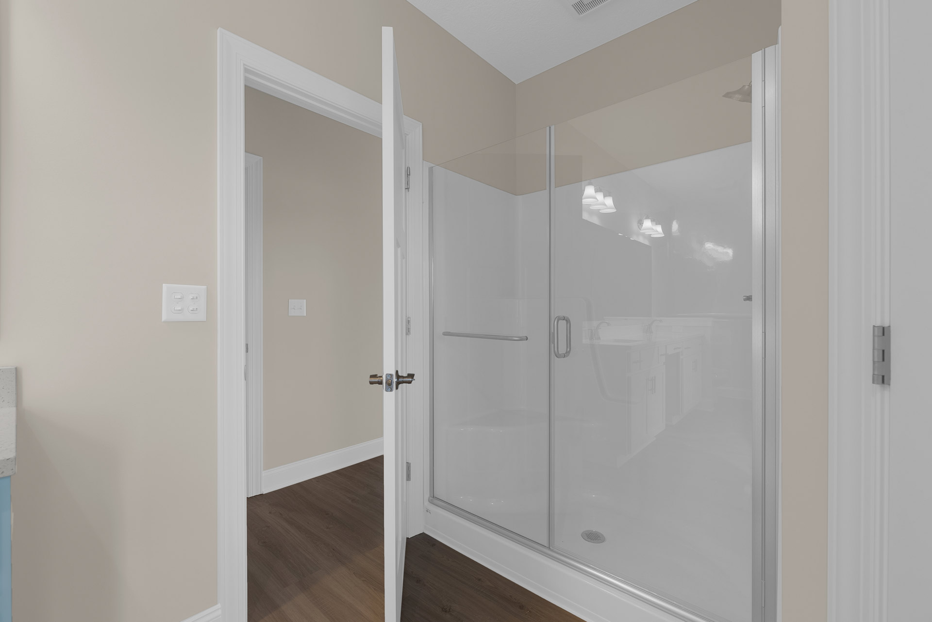 Bathroom with glass shower enclosure, wood flooring, white trim, and plaster walls; modern light fixture and light switch visible.