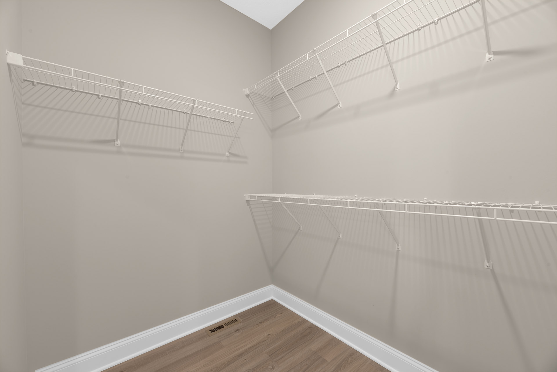 White built-in shelves against a plaster wall, wood floor with a vent, and ceiling detail in a bright indoor room.