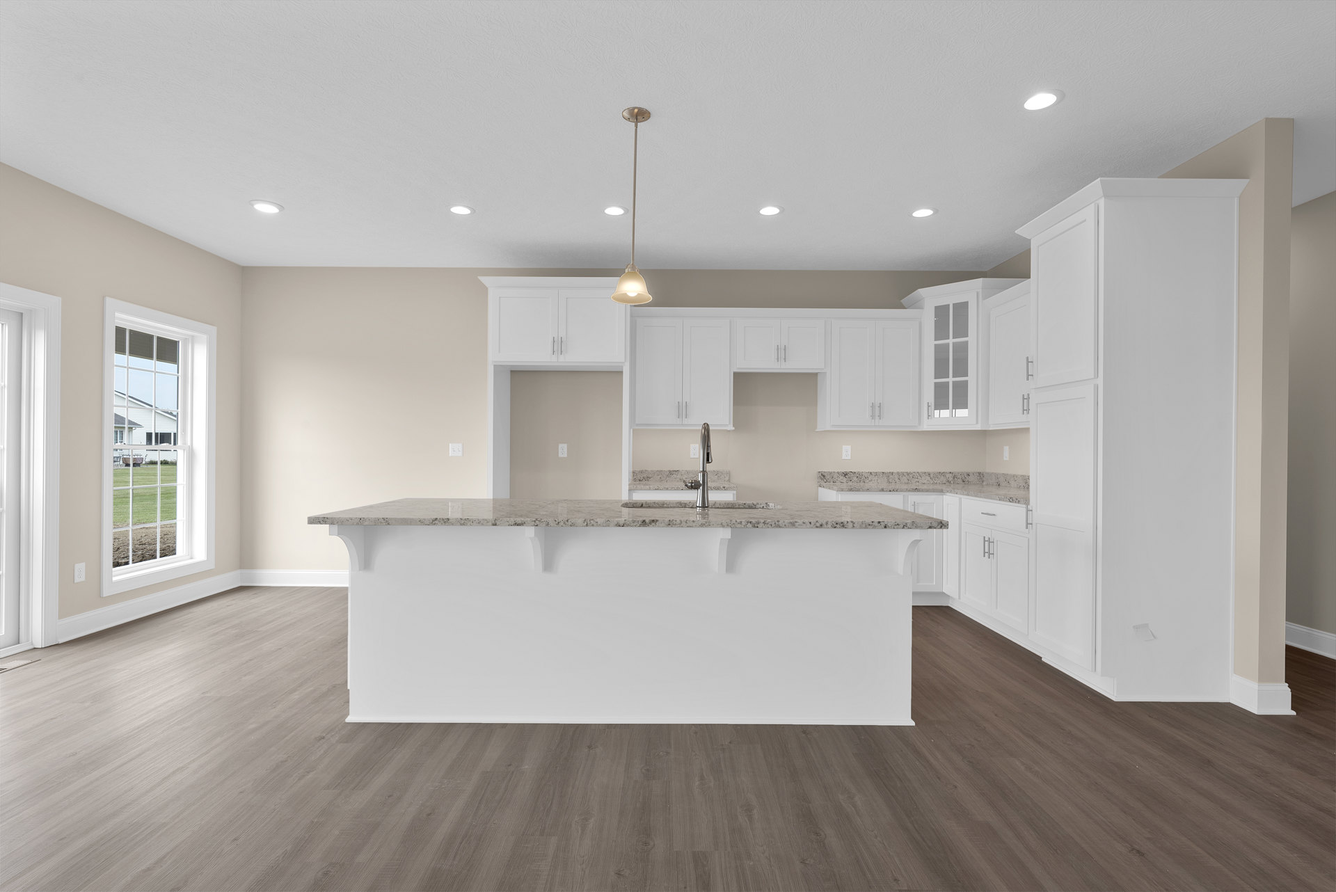 Spacious kitchen featuring a marble island with built-in sink, wood flooring, white walls, ceiling light fixture, cabinetry, and a window overlooking a green lawn and neighboring