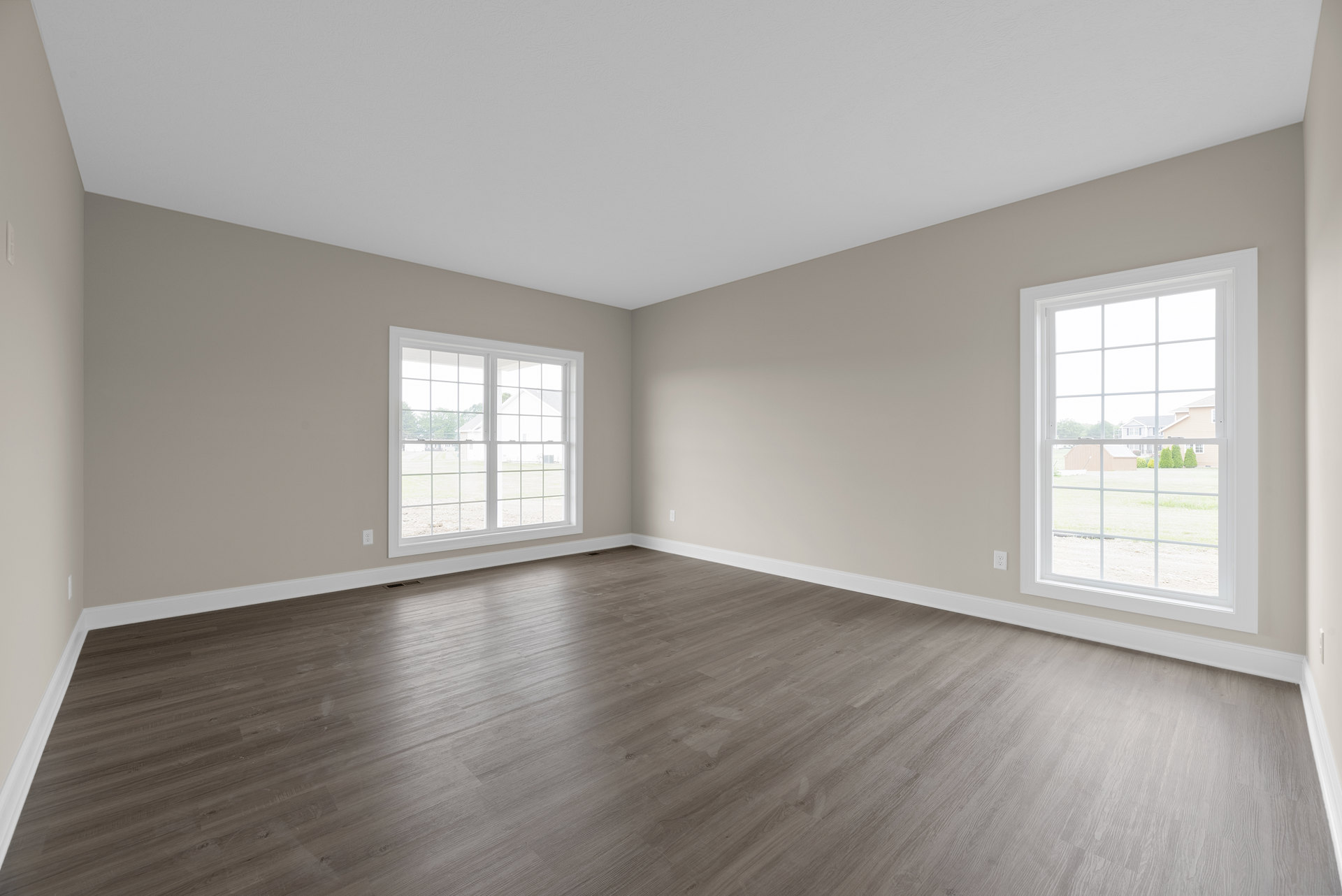 Sunlit room featuring wide plank wood flooring, large multi-pane windows, white plaster walls, and a view of a landscaped yard.