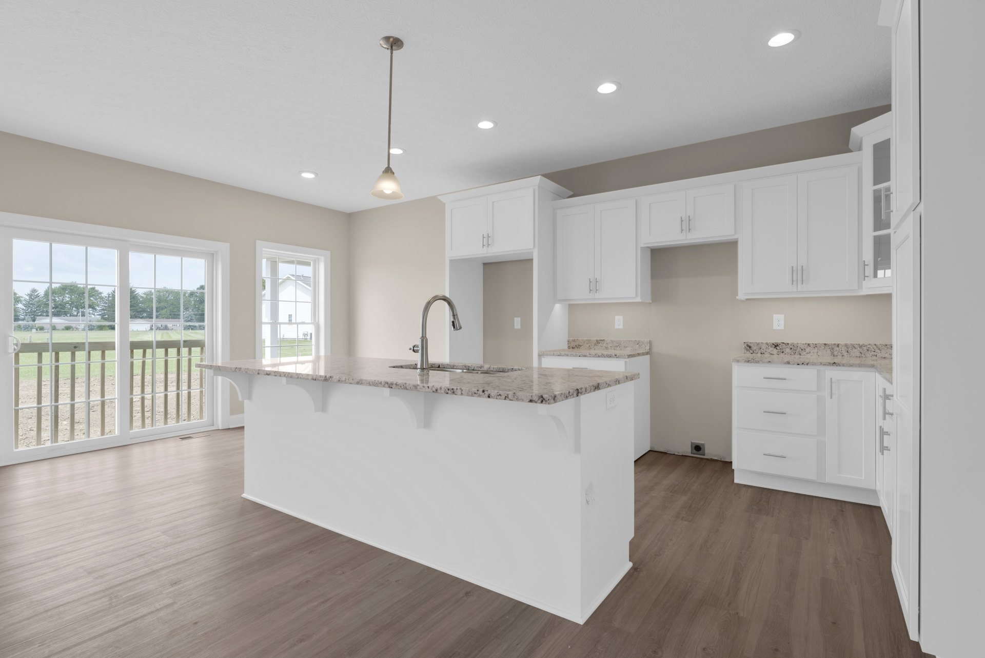 Spacious kitchen featuring a large central island with stone countertop, built-in sink and metal faucet, light wood cabinetry, sliding glass door opening to grassy field, and