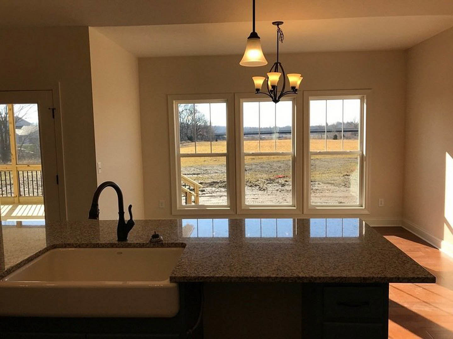 Modern kitchen featuring a large window, tile backsplash, stone countertop, stainless steel sink and faucet, and a chandelier suspended above the workspace.