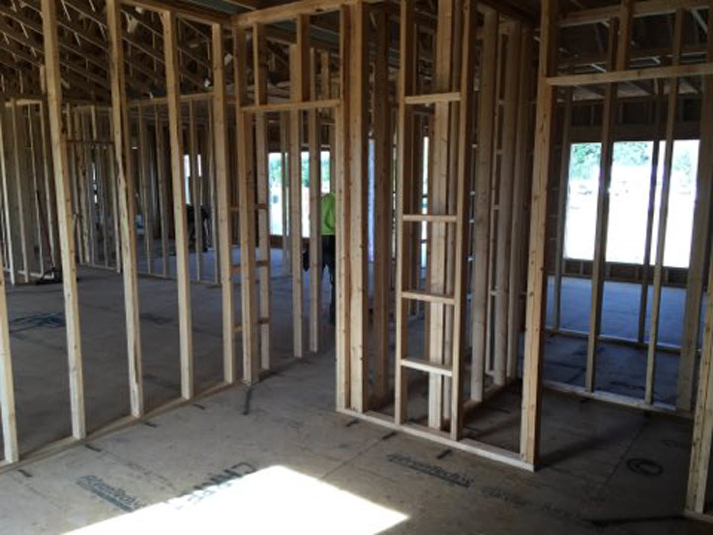 Framed window with clear glass pane in unfinished wood interior, construction worker standing on plywood floor, exposed beams and lumber visible