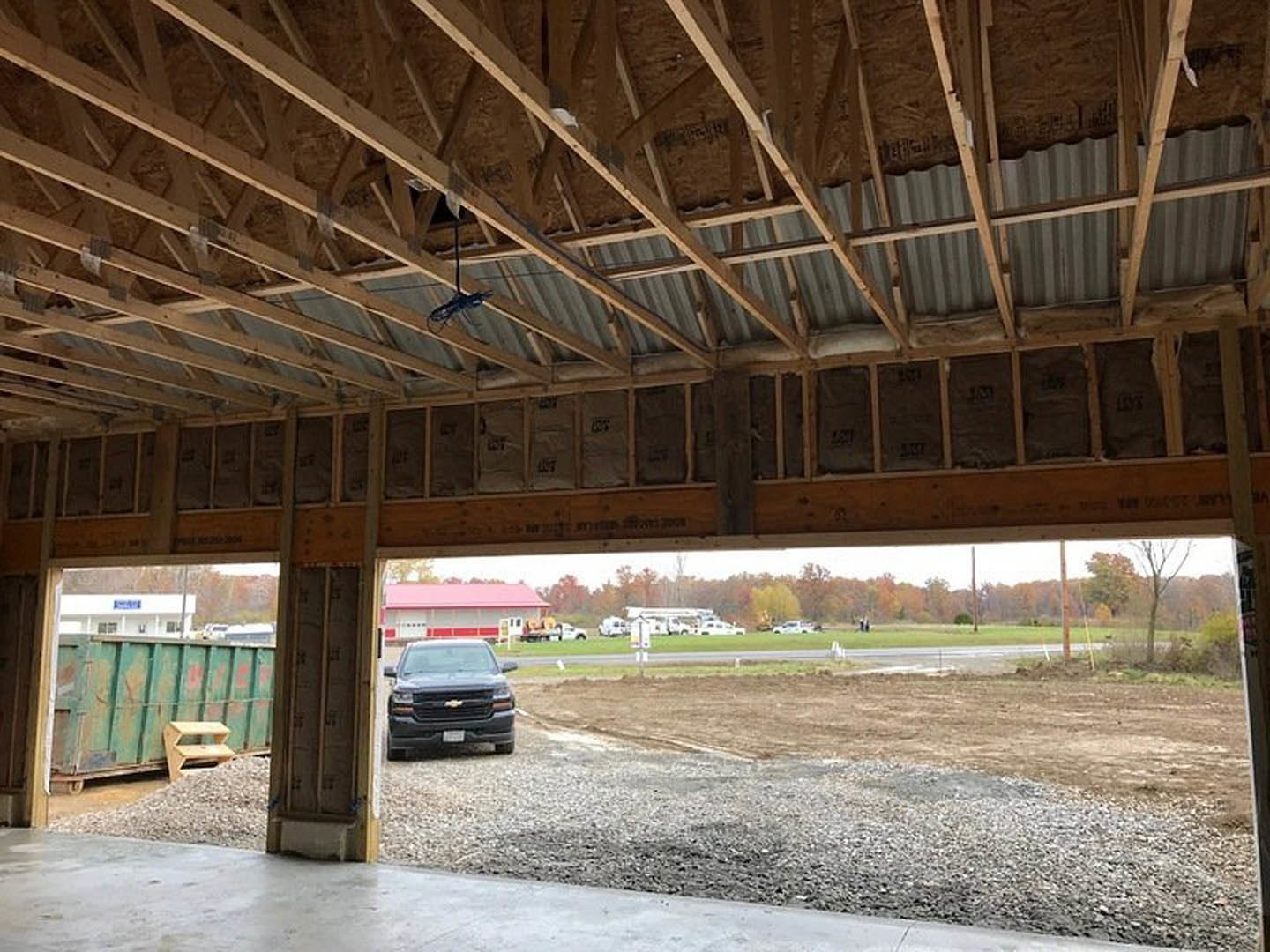 Black pickup truck parked on concrete driveway in front of custom home with red roof, exposed wooden beams, and green dumpster nearby.