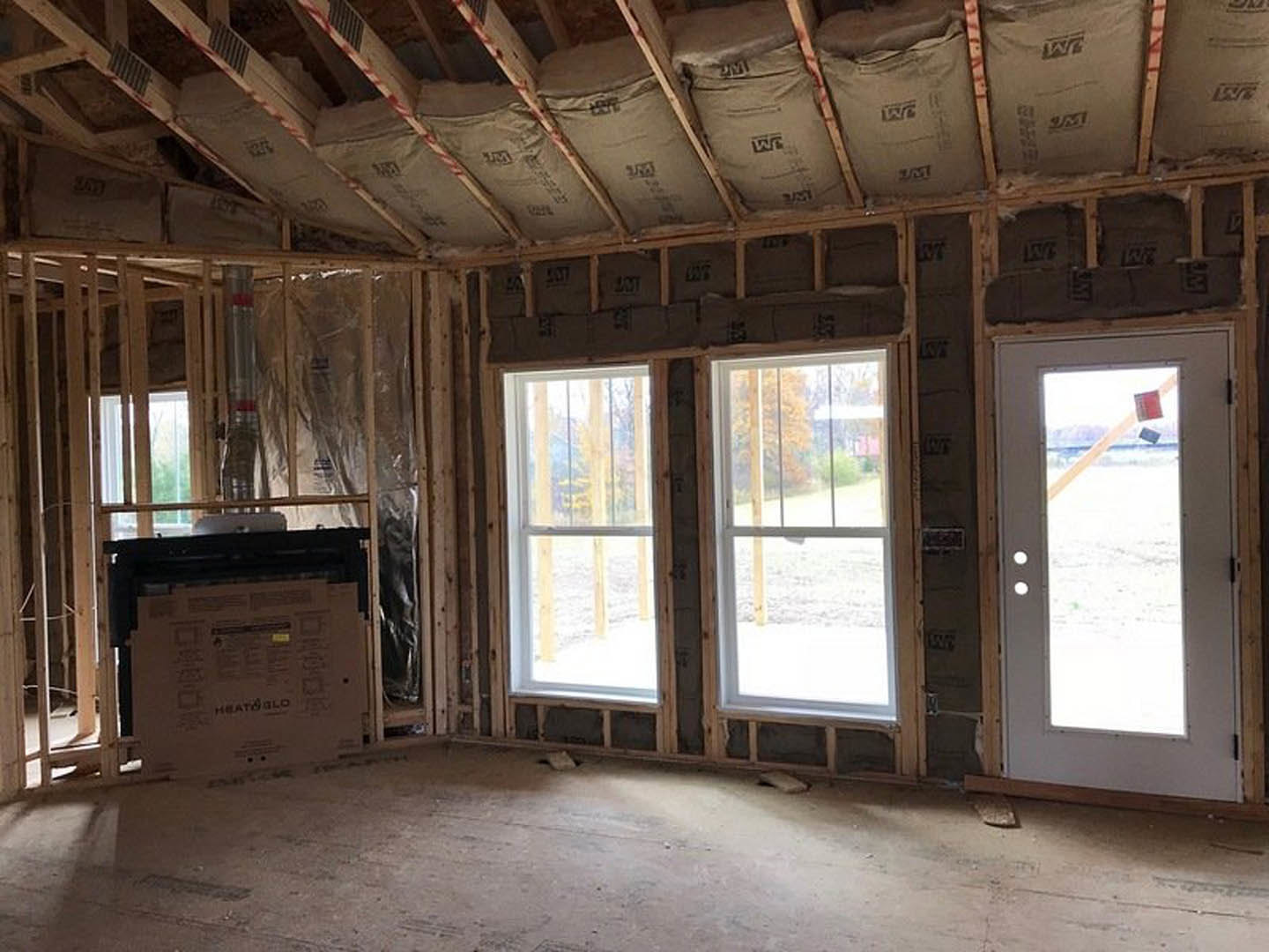 Bright room with white plaster walls, wood ceiling beams, two large windows, and a paneled door; cardboard moving box and bags on a shelf visible.