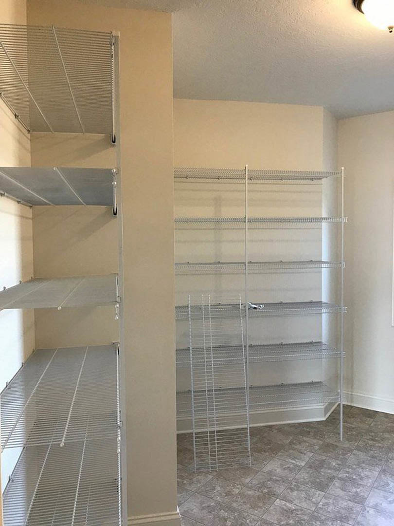 Built-in white shelves along a plaster wall, grey tile flooring with white baseboard trim, metal railing and glass door visible in a modern interior room.