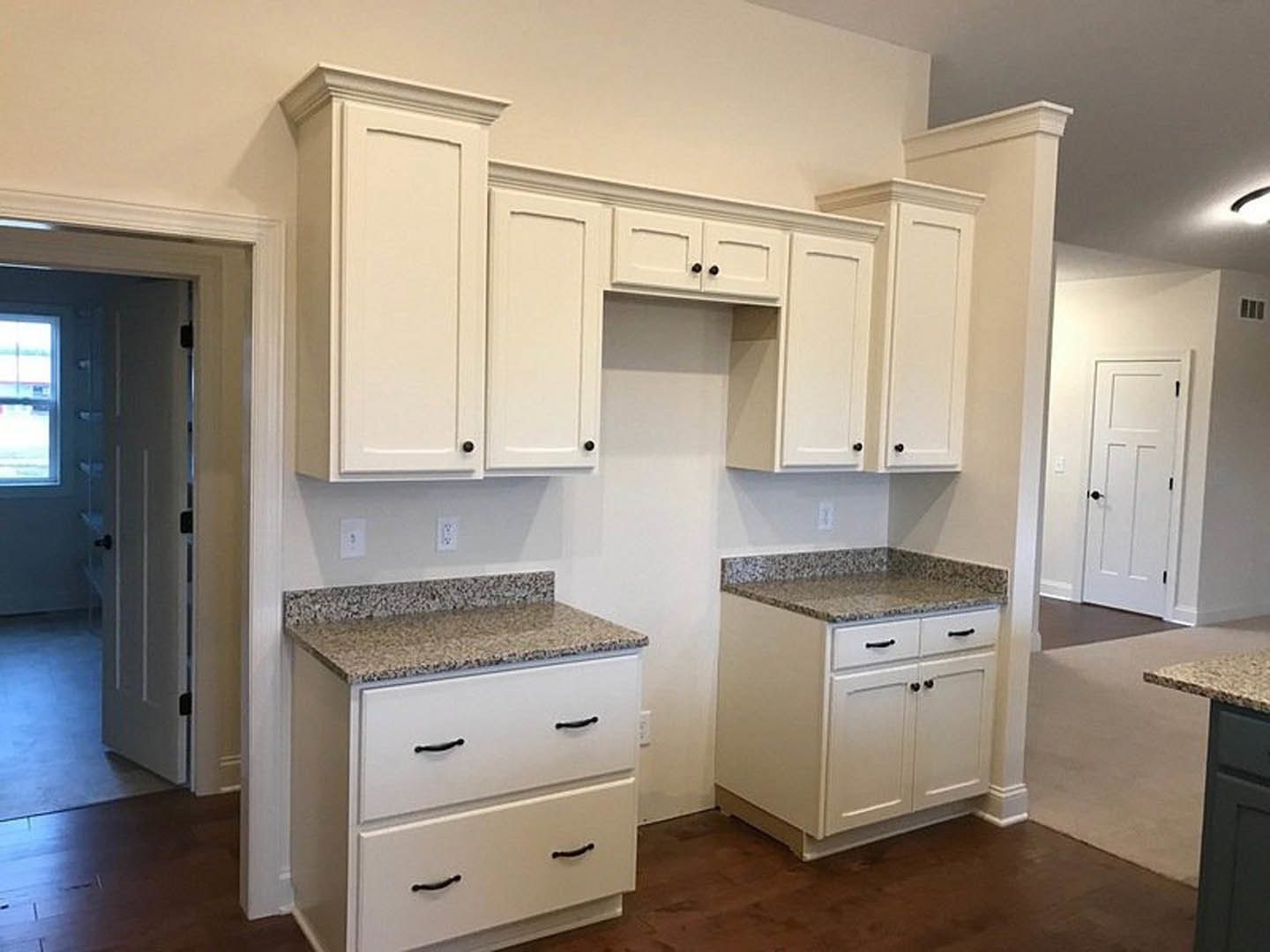 White kitchen cabinets with black knobs, granite countertops, stainless steel sink, white drawers, and light-colored flooring