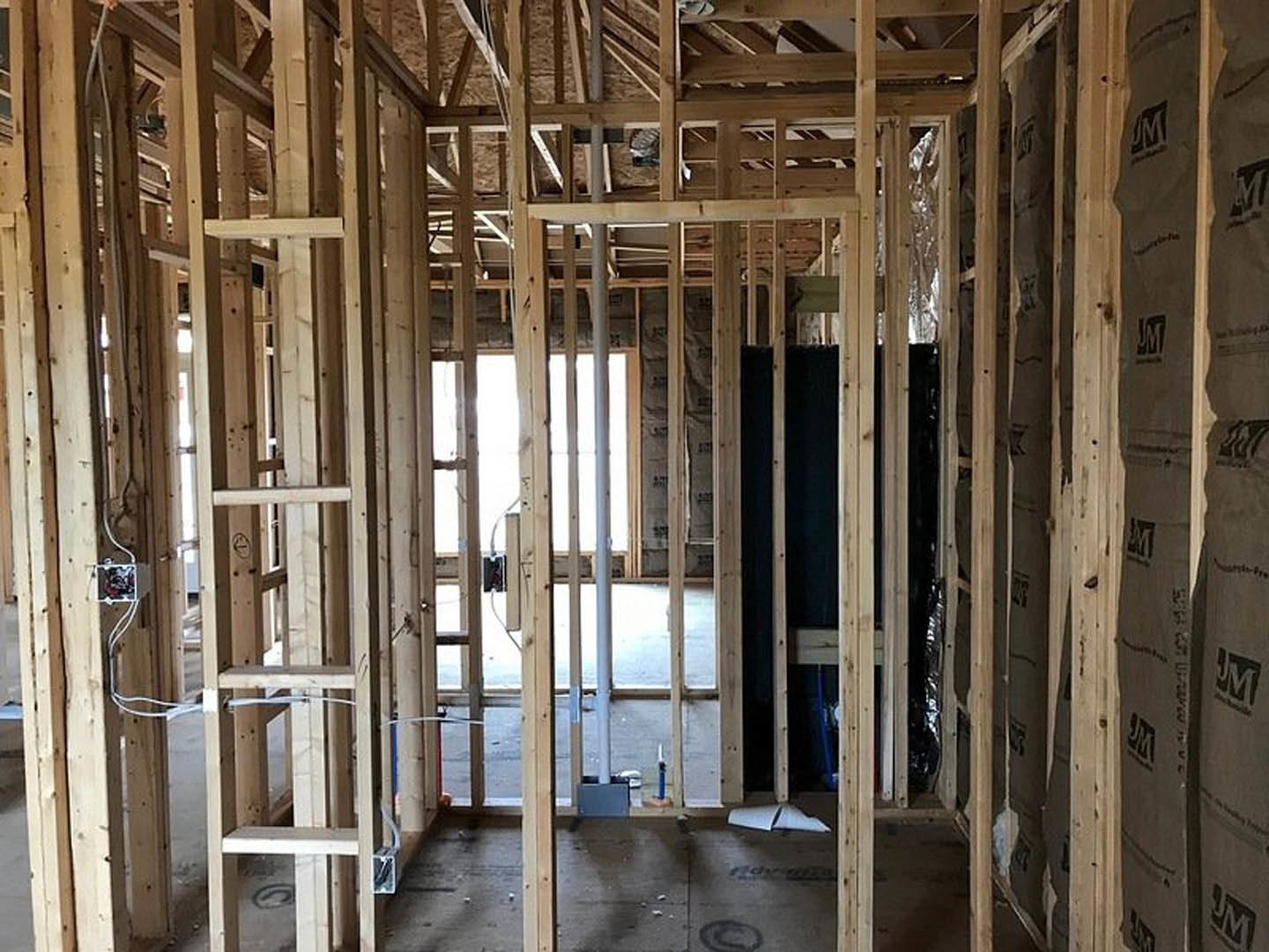 Exposed wood framing and beams inside a house under construction, with visible lumber, insulation, and partially finished walls