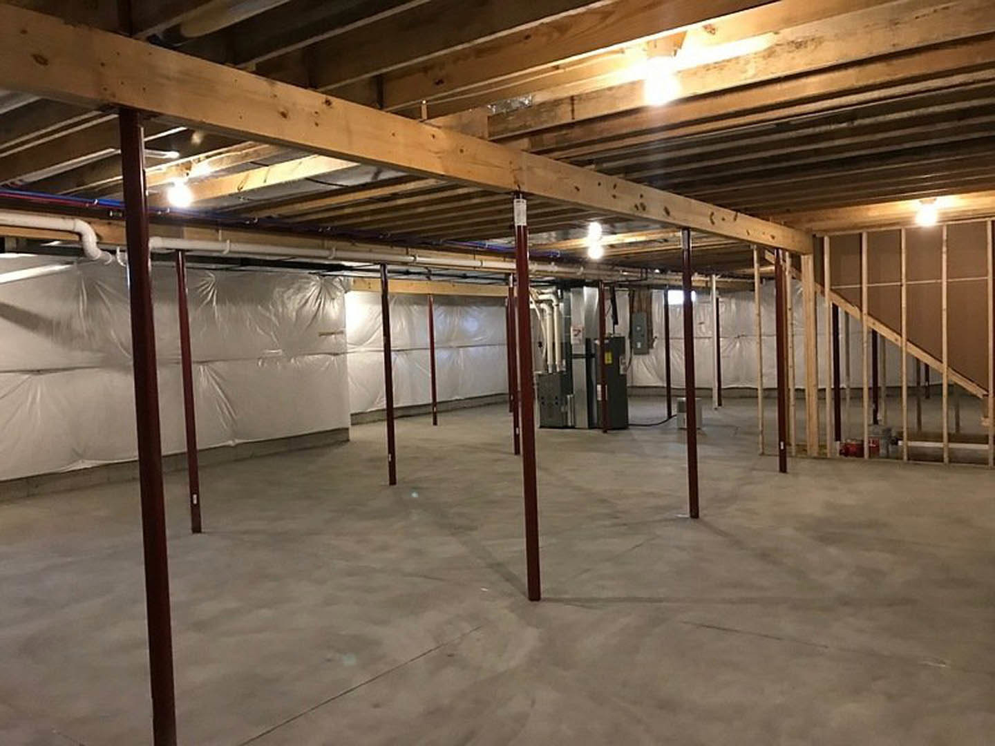 Exposed wooden ceiling beams and steel support poles over a concrete floor, white plastic sheeting covering one wall, red metal pillar in foreground