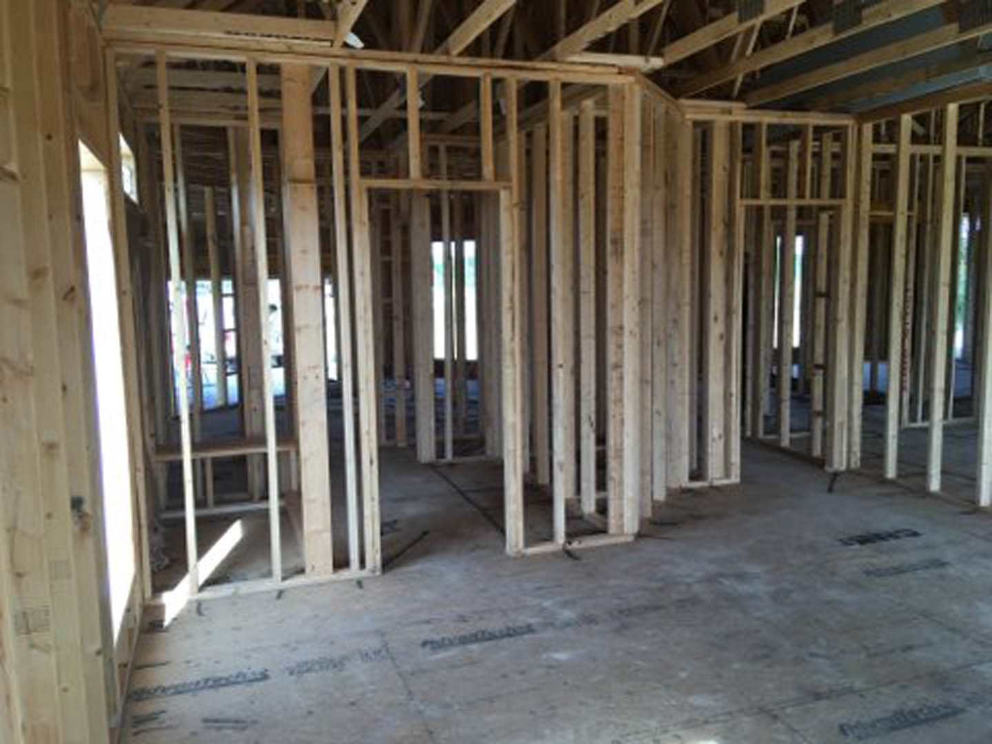 Exposed wood framing and beams inside a partially constructed home, with unfinished floors and a cloudy sky visible through open walls