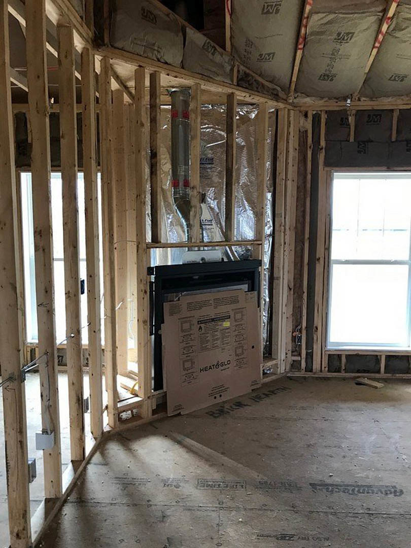 Living room with wood beam ceiling, large window, stone fireplace, unfinished walls, and cardboard box on hardwood floor