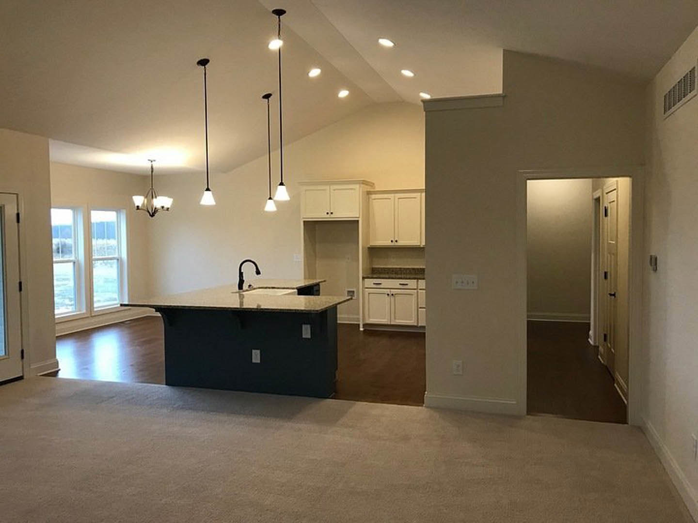 Open-concept kitchen and living room featuring a large island with white cabinetry, black faucet, stone countertop, tile flooring, and carpeted seating area near expansive windows.
