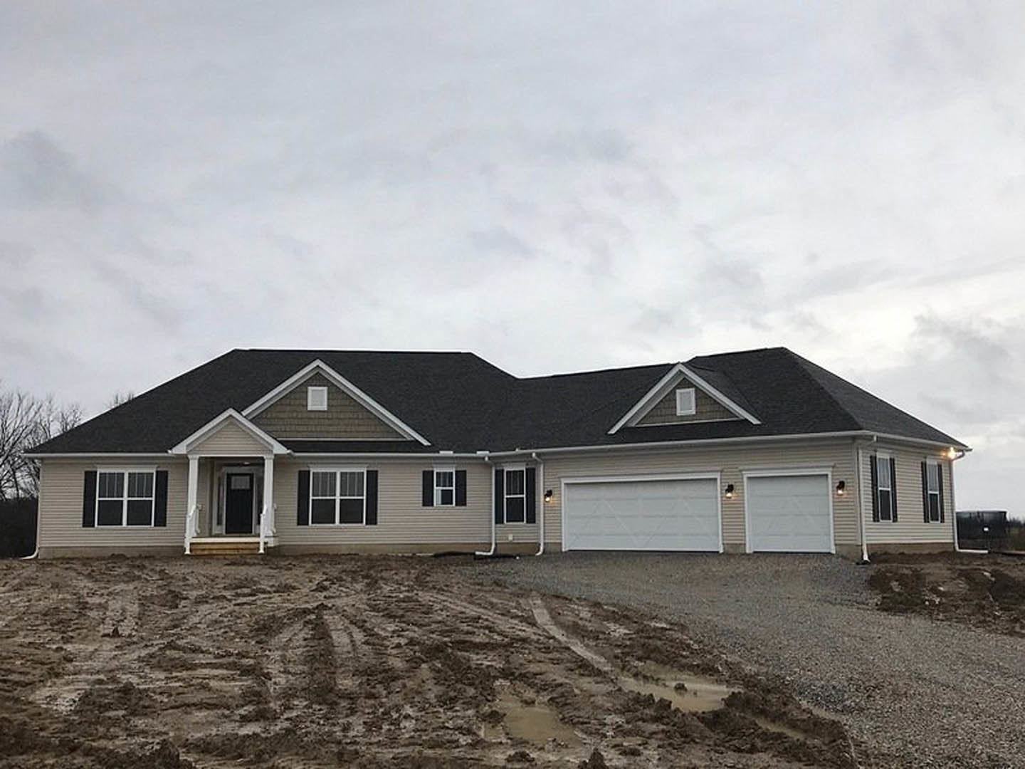 White modern house with black roof, metal-framed white walls, two driveways, large garage door, and windows with white trim under a partly cloudy sky
