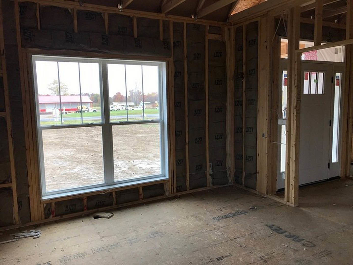 Bright room with wood beam ceiling, white walls, large window overlooking red and white building, white door, hardwood floor