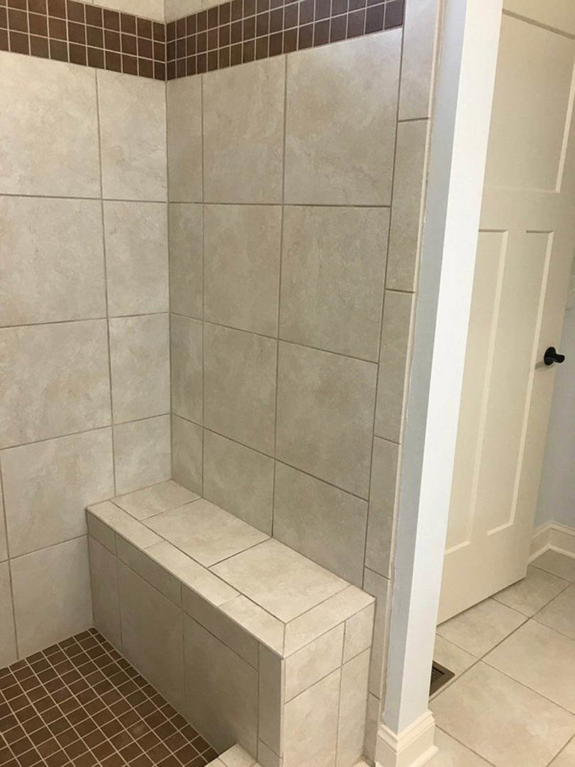 Brown tiled shower with built-in bench, matching tile walls and floor, white door visible in corner