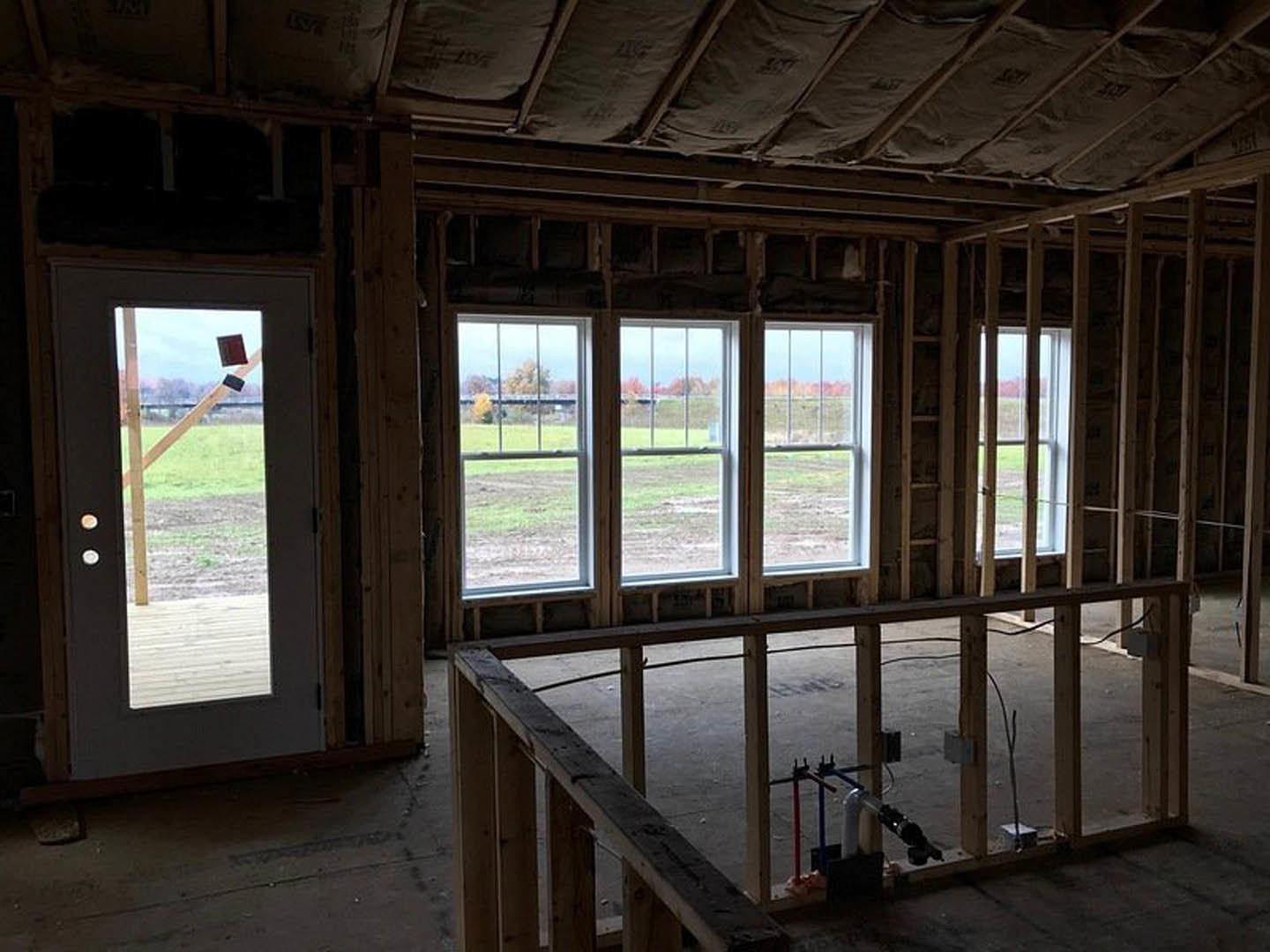 Wood-beamed ceiling and hardwood floor in a bright room featuring a door and large windows overlooking a grassy field and trees