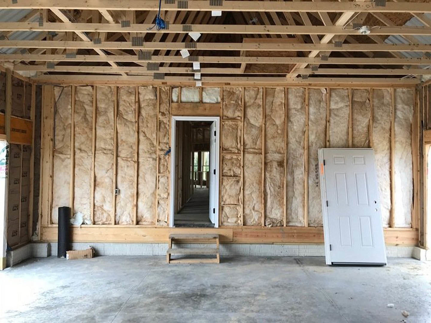 White door set in a wood-paneled wall, exposed wooden ceiling beams, light-colored floor, and construction materials visible in the room.