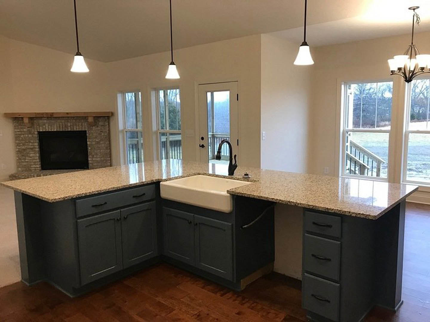 Open-concept kitchen featuring granite countertops, stainless steel sink, white cabinetry, hardwood flooring, and a modern fireplace with a black screen integrated into the wall.