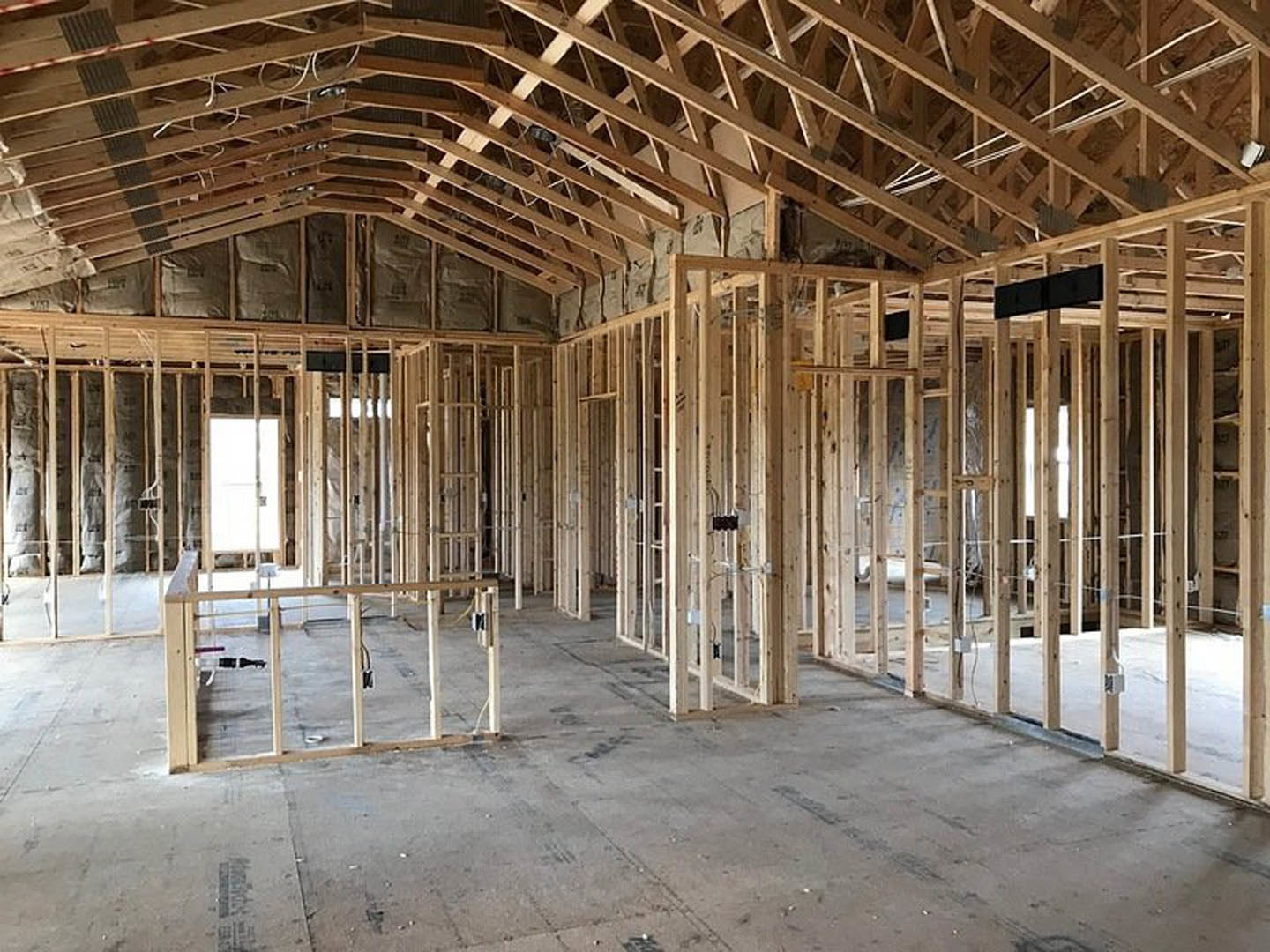 Wood framing and exposed beams inside a residential construction site with unfinished floors and ceiling
