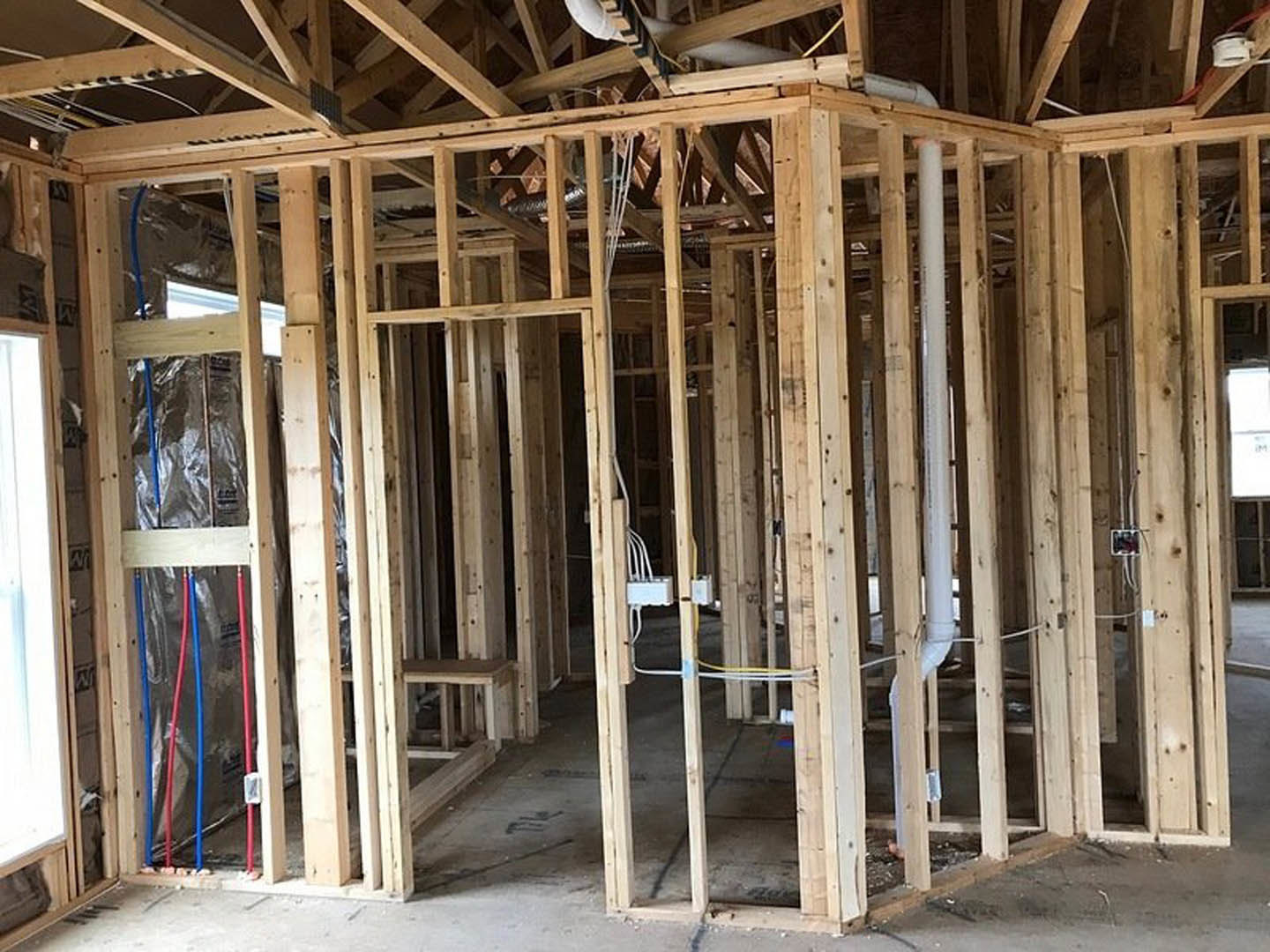 Exposed wood framing with electrical wires and a white electrical box mounted between beams during home construction