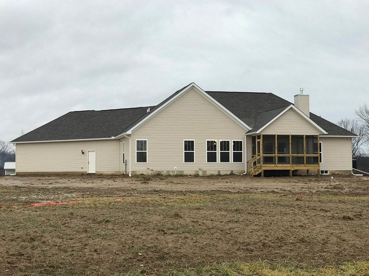 White cottage-style house with covered porch, white-framed windows, horizontal siding, and expansive grassy yard under partly cloudy sky