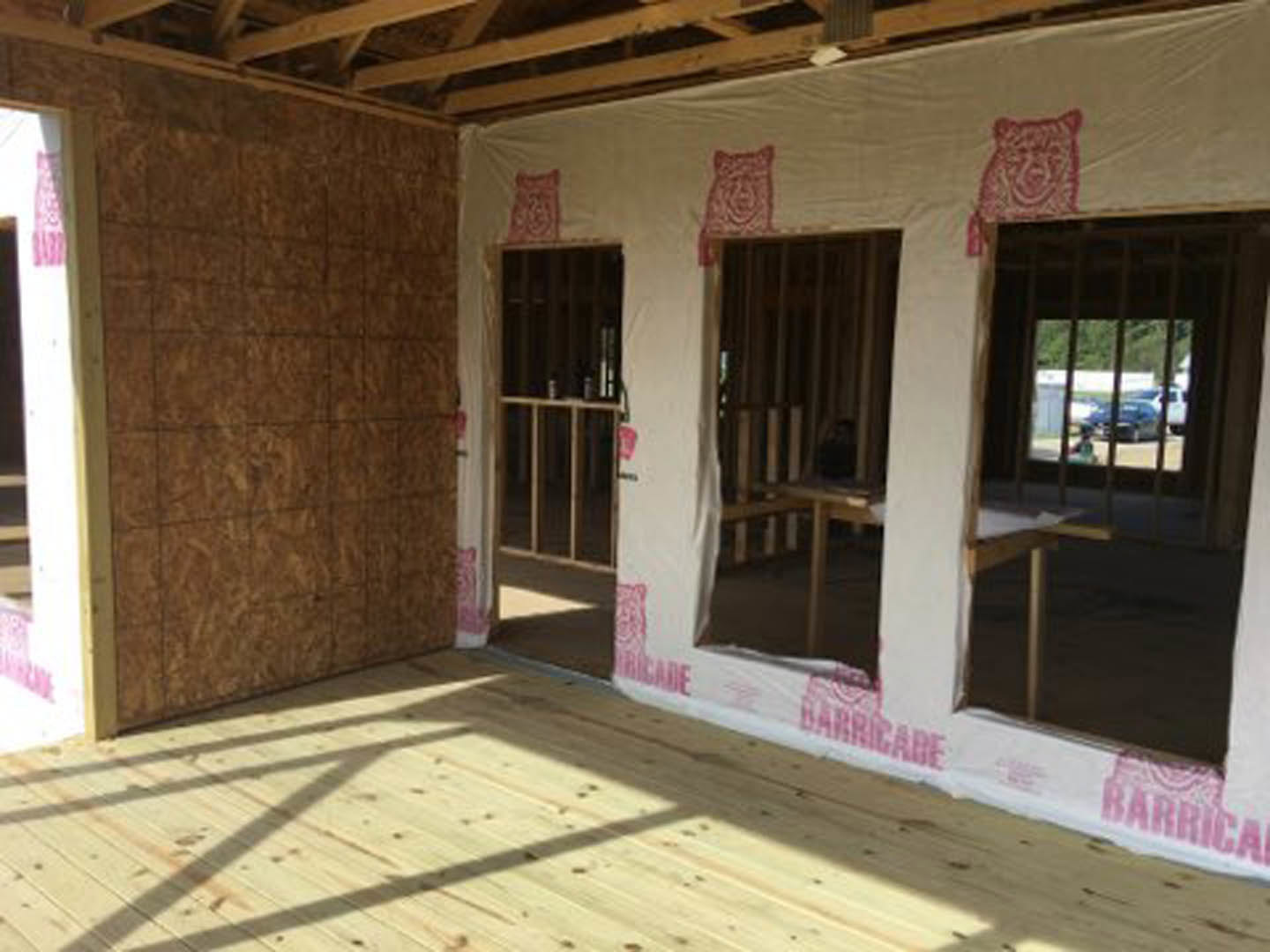 Sunlit room with light wood flooring, large window with metal bars, white tiled wall, and visible construction elements