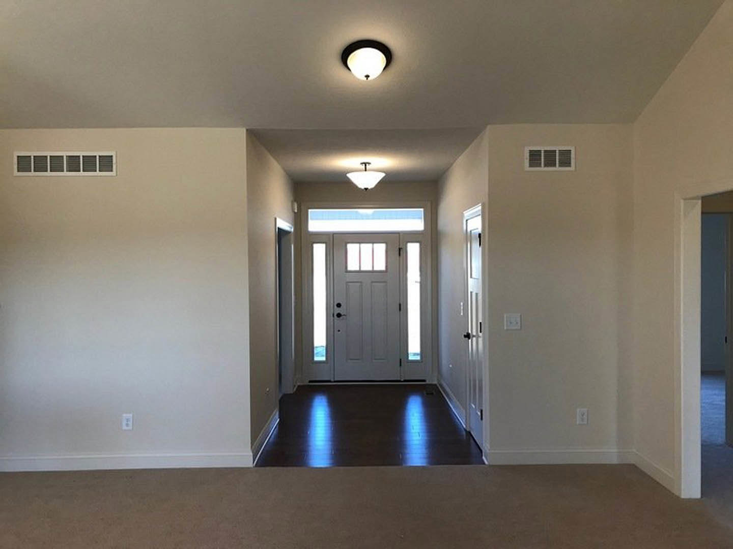 Hallway with white paneled door and adjacent glass door, light fixture on plaster ceiling, carpeted floor, blue accent light on black surface