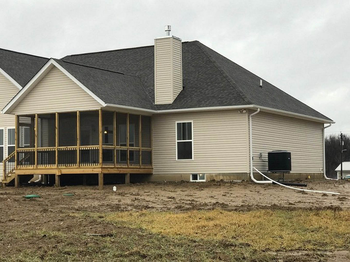 White cottage-style home with black roof, white-framed windows, covered front porch, wooden deck, and dirt landscaping under a partly cloudy sky