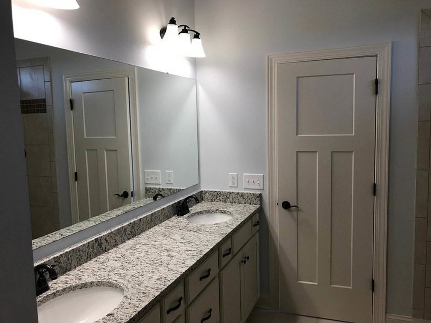 Bathroom with double vanity featuring undermount sinks, quartz countertop, white cabinetry, black hardware, and a white door with black handle; tile flooring and modern light