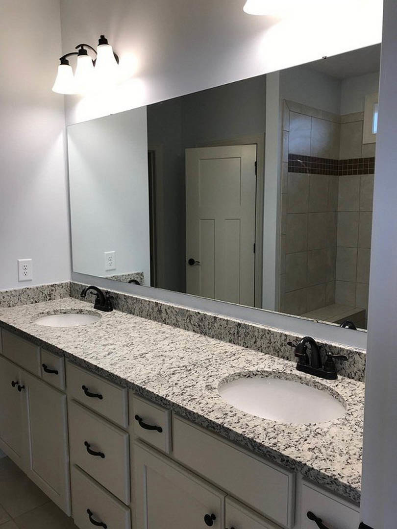 Bathroom with a large mirror above a marbled countertop, black faucet, white circular sink set in stone, white door with black hardware, three-light fixture, tile walls, and