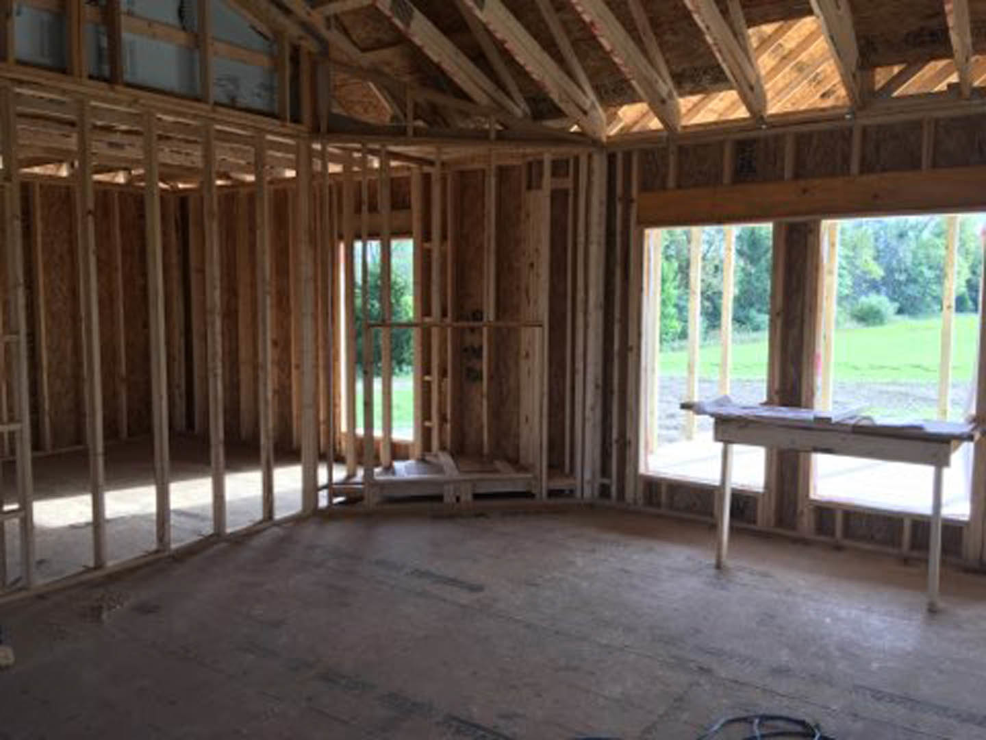 Sunlit room featuring a wooden table on hardwood plank flooring, large window framed by exposed wooden beams, and minimalist interior design.