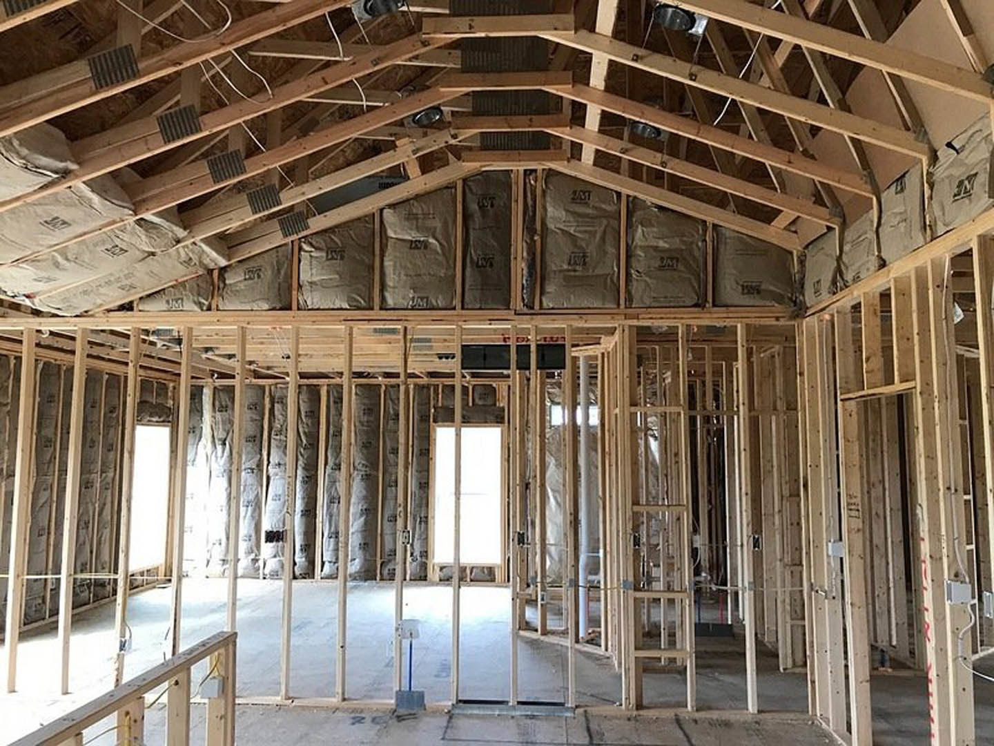 Exposed wood ceiling beams, unfinished walls, large window, metal floor grate, construction materials including brown paper bags with black writing.