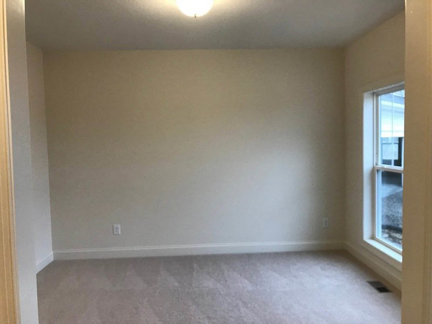 Bedroom with soft grey carpet, white walls and ceiling, single window with white frame, wall-mounted light fixture