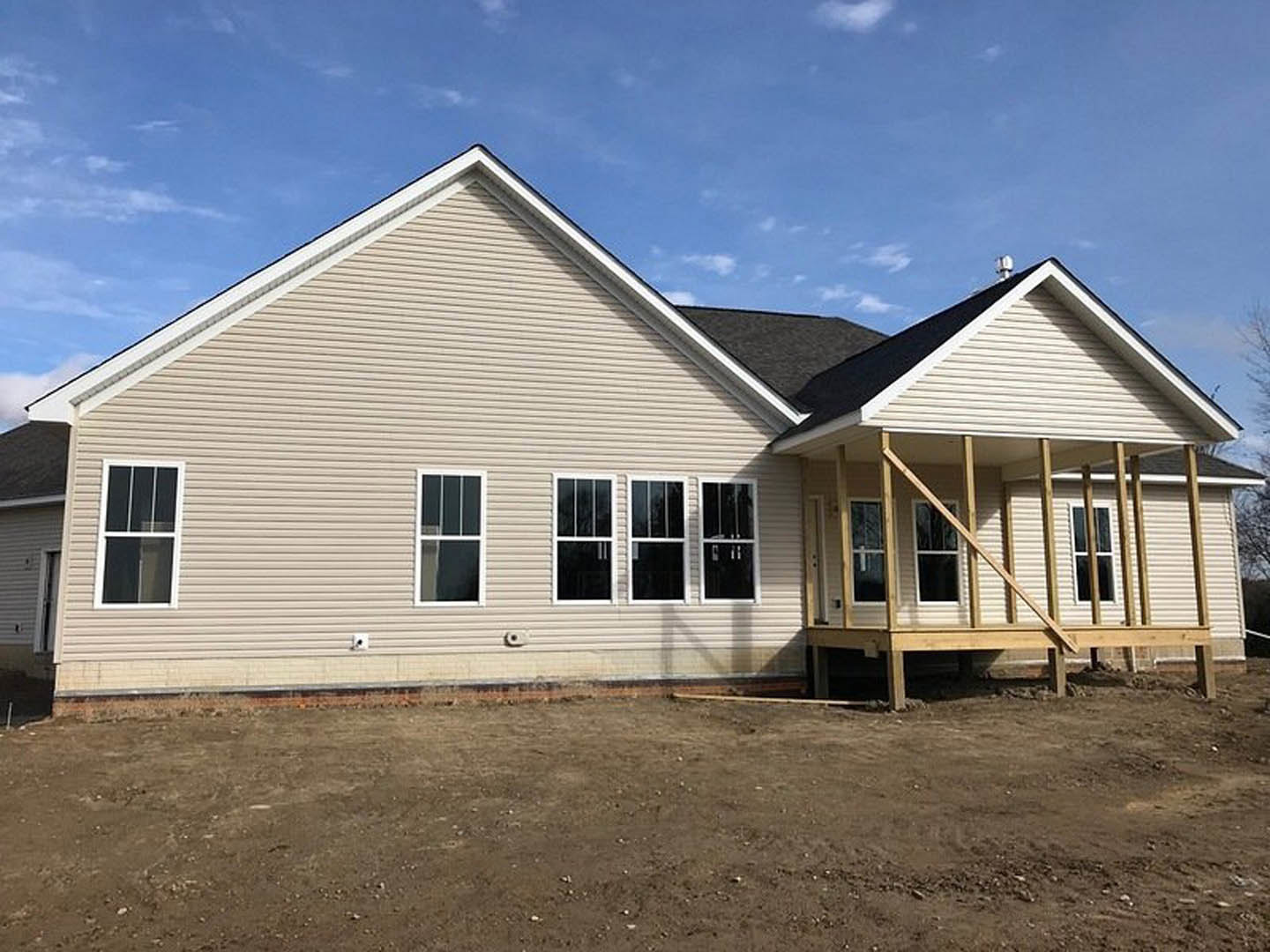 Wood-framed porch attached to a partially finished house with white window frames, exposed siding, and dirt construction area in foreground