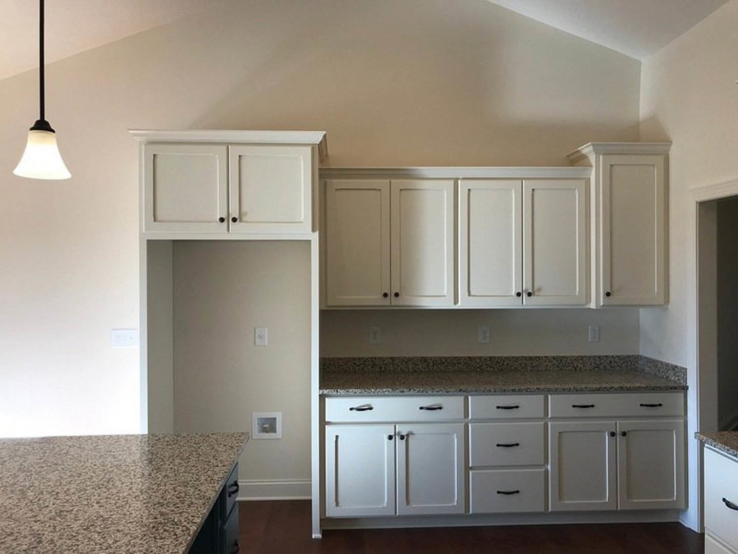 White kitchen cabinets with black knobs, granite countertops, stainless steel appliances, and light-colored flooring