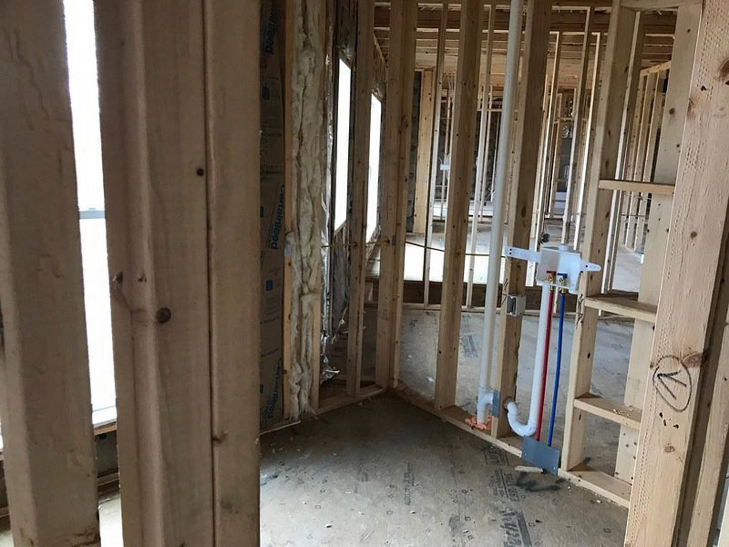 Unfinished room with exposed wood framing, white pipe running along wall, window letting in natural light, construction materials visible