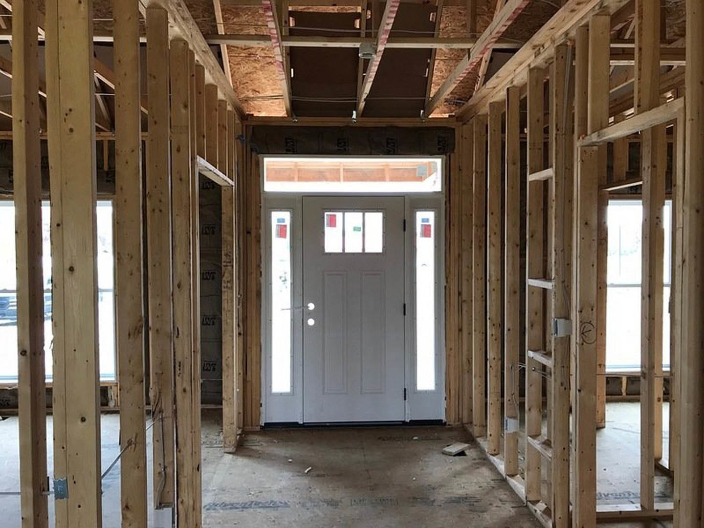 Framed doorway with white door and glass window, exposed wooden beams, unfinished walls, and visible construction materials