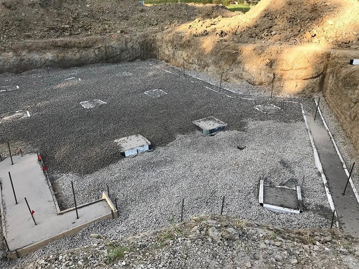 Concrete foundation slabs with exposed metal rebar surrounded by gravel and soil at a residential construction site