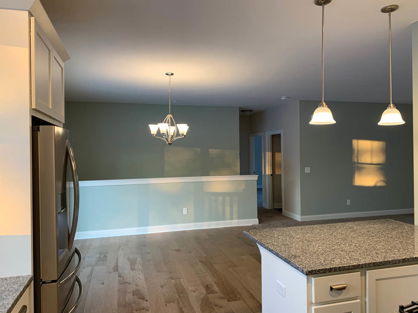 Spacious kitchen featuring a large central island with stone countertop, stainless steel refrigerator, white cabinetry, tile backsplash, and wood flooring