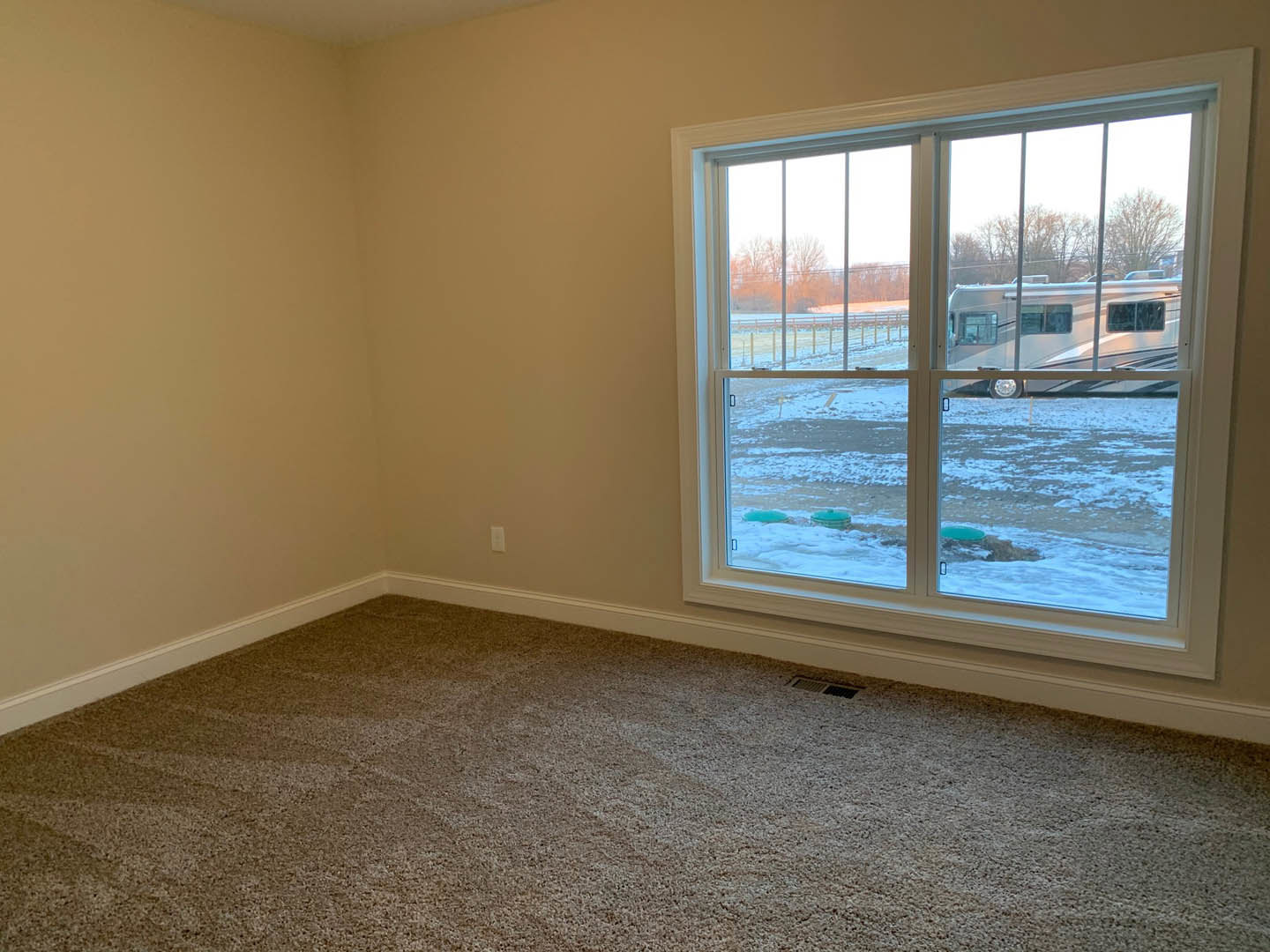 Carpeted room with a large window, white walls, and a view of a camper parked outside on snowy ground