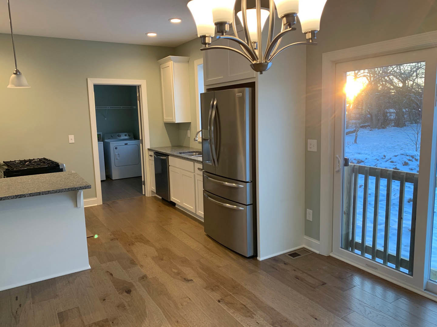 Modern kitchen featuring white cabinetry, stainless steel refrigerator, glass door leading to snowy landscape, light fixture above stone countertops, window with view of
