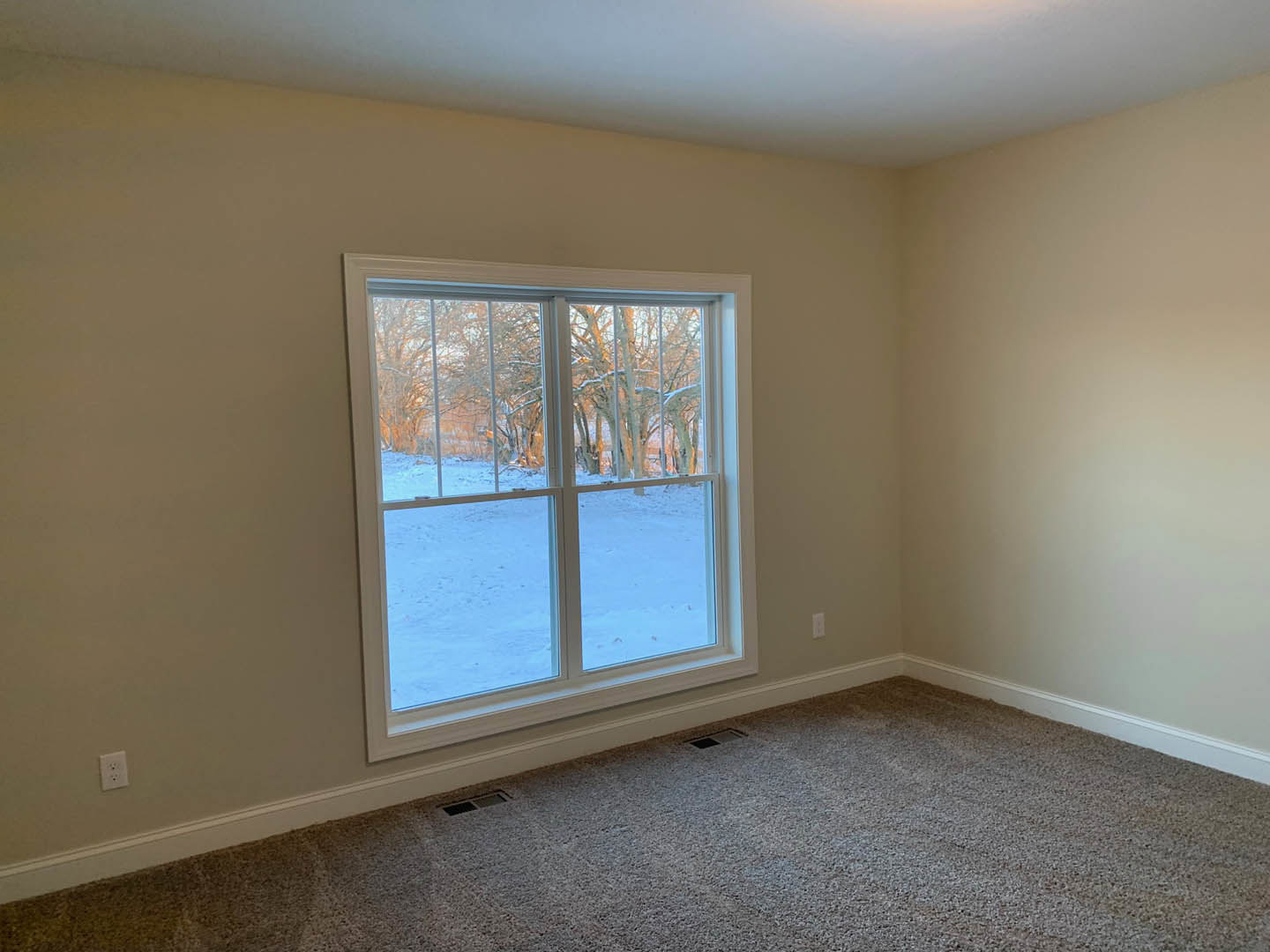 Carpeted bedroom with large window overlooking snowy landscape, white ceiling, wall vent, and window blinds