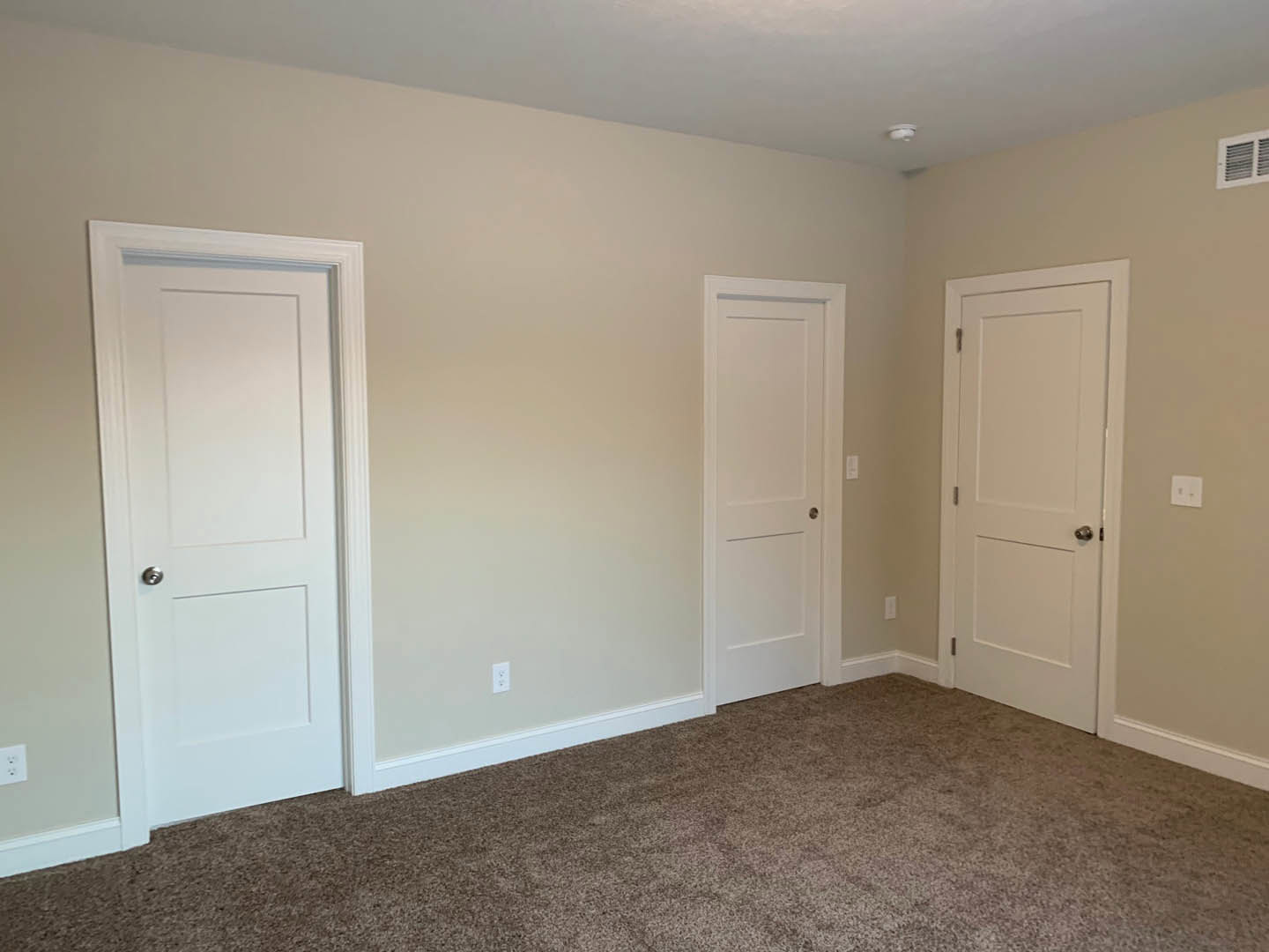 Bedroom with two white paneled doors, silver handles, light beige carpet flooring, and a wall vent
