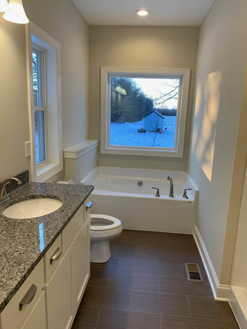 Bathroom with brown tile floor, white sink and chrome faucet, window overlooking snowy yard, wall vent visible near baseboard