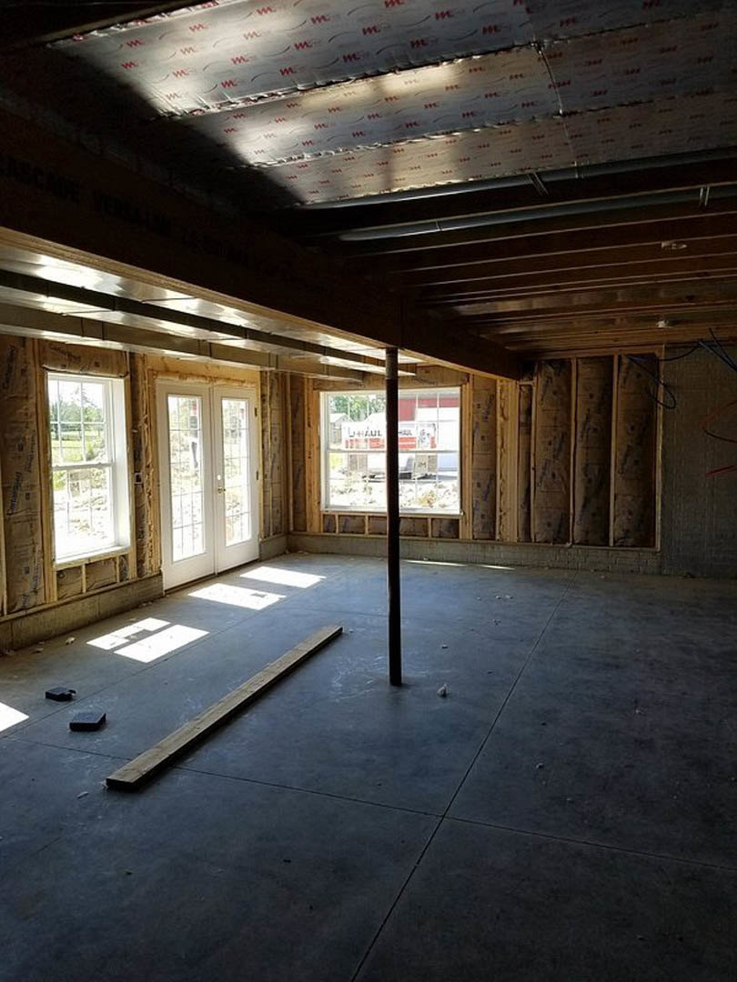 Concrete floor with a central wooden support beam, white double doors with glass panes, white ceiling, and window providing daylight and outdoor view