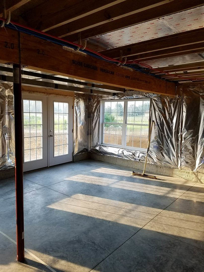 Wood-beamed ceiling and double glass-paneled doors in a sunlit room with multi-pane windows, light wood flooring, and a mop near the entrance