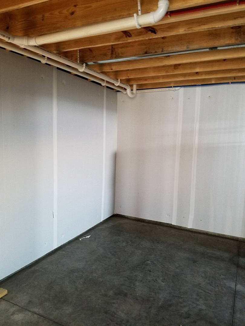 Concrete floor with exposed ceiling pipes, white plaster walls, and unfinished wood surfaces