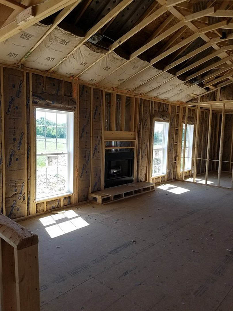Living room with exposed wood beams, white square tile flooring, stone fireplace, and large window letting in natural light