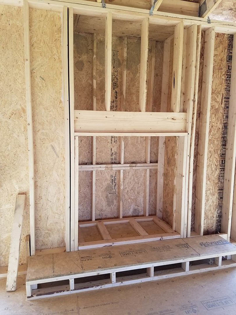 Wooden frame with white paint resting on tile floor, surrounded by plywood and hardwood planks in an unfinished interior room.